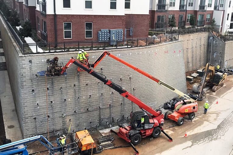 Workers on a lift performing maintenance or stabilization on a tall retaining wall.
