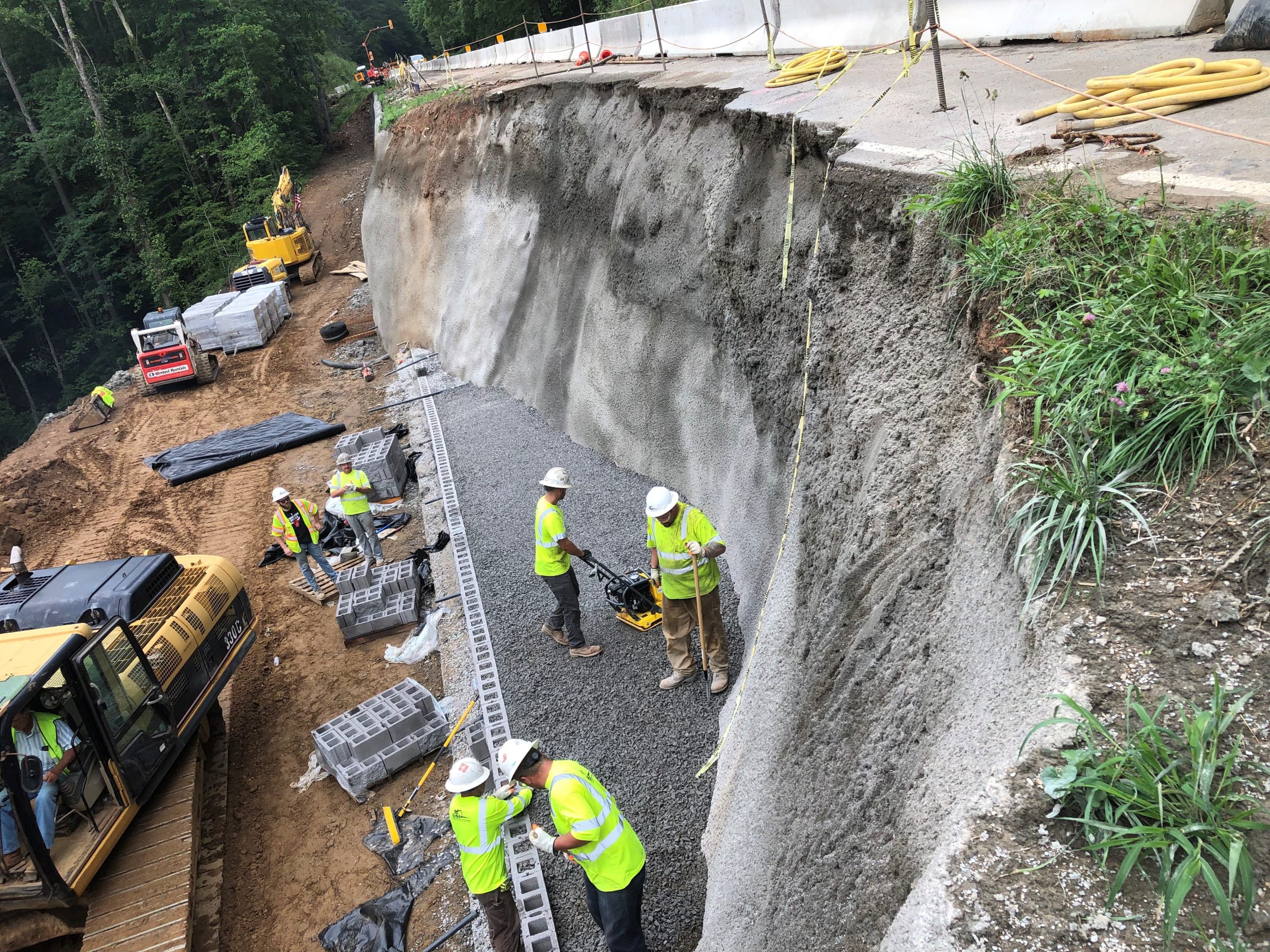 Construction crew repairing a roadside embankment with shotcrete walls.
