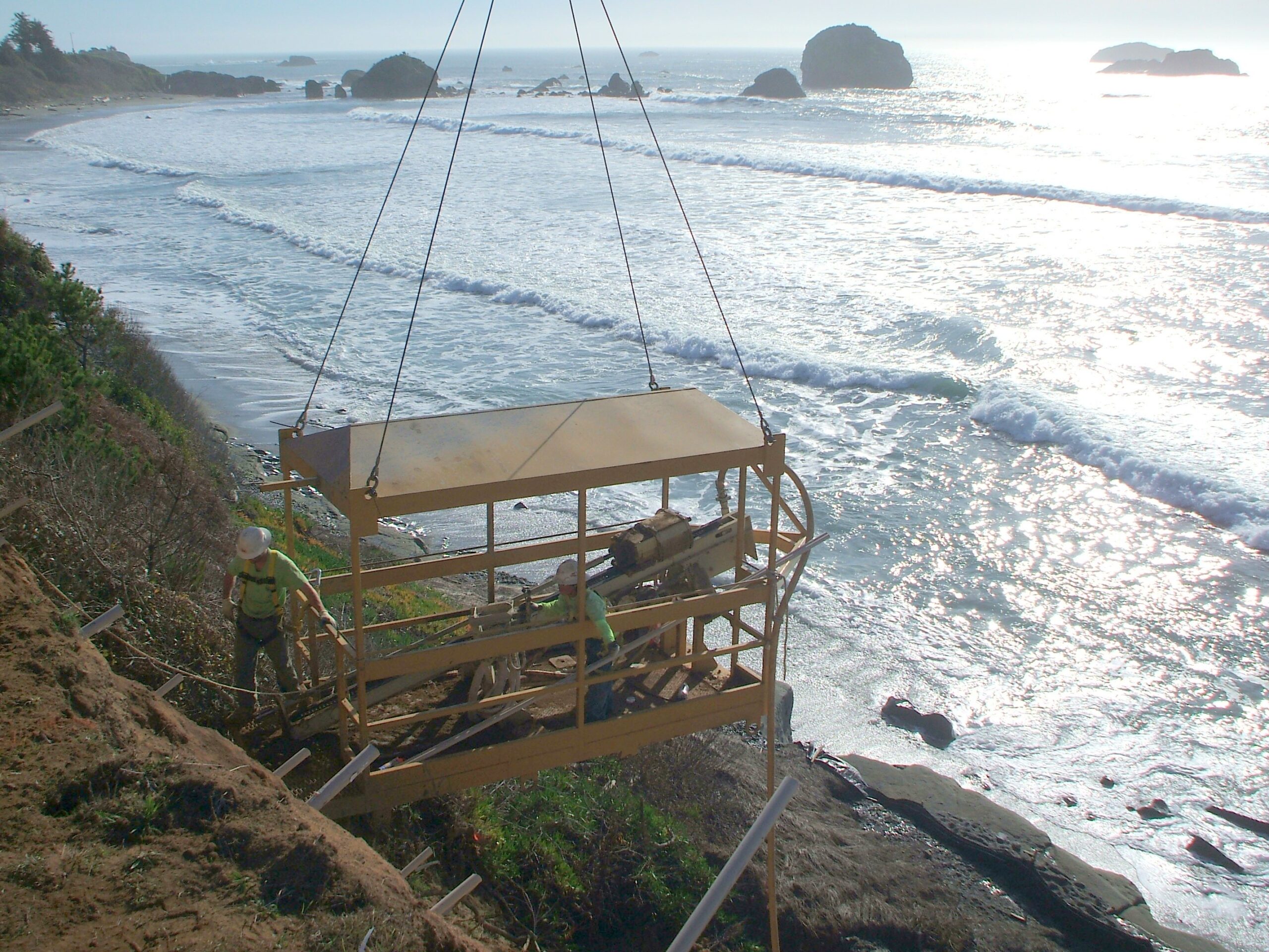 Suspended work platform hanging over coastal cliff during shoreline stabilization.