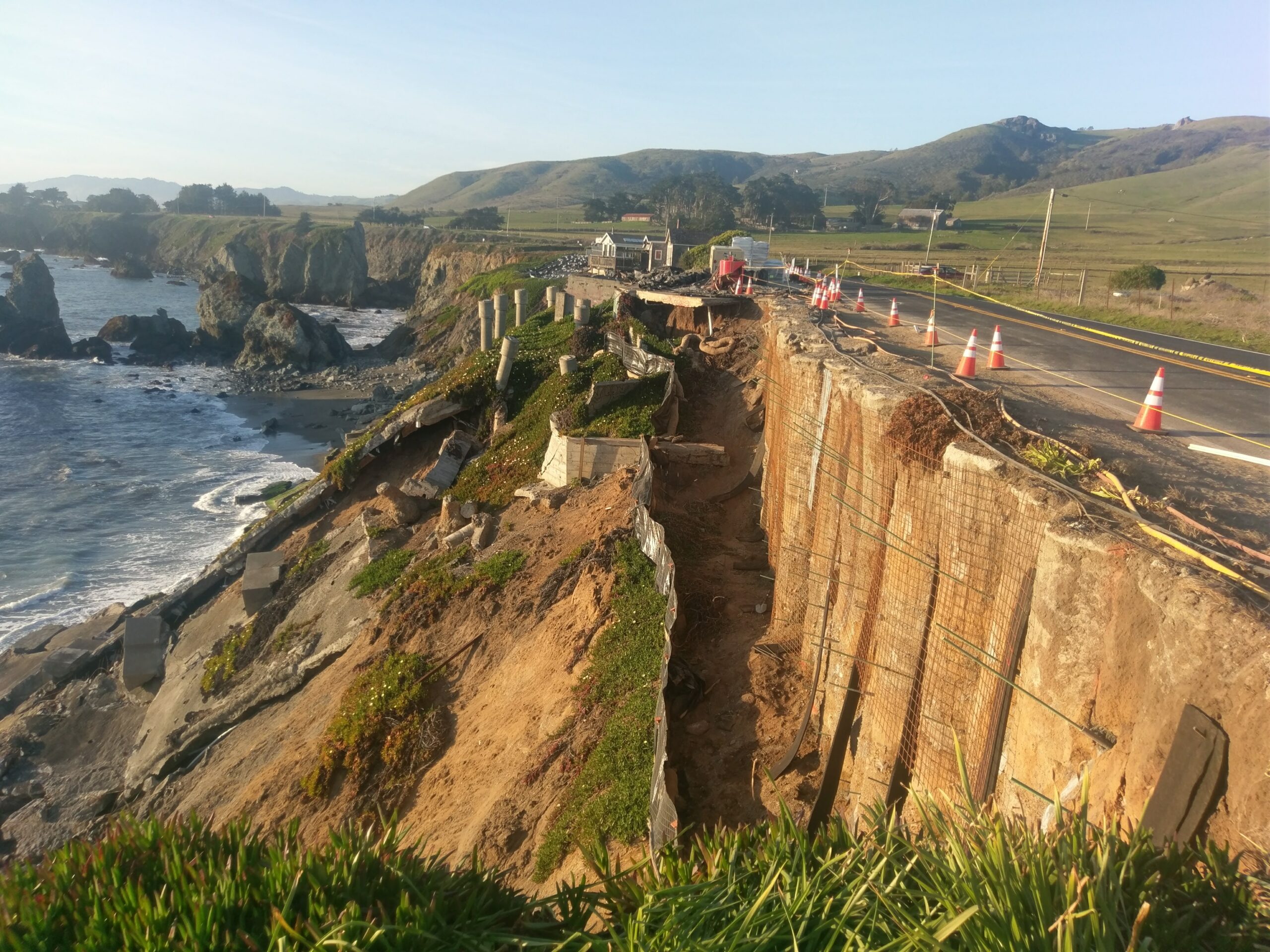 Coastal highway partially collapsed from cliff erosion near the ocean.