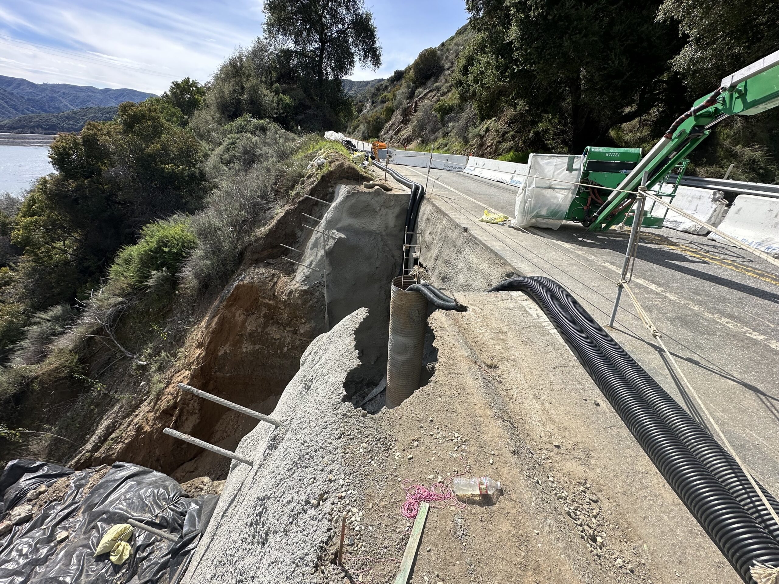 Roadside landslide repair in progress with exposed soil nails and shotcrete wall supporting the slope below.