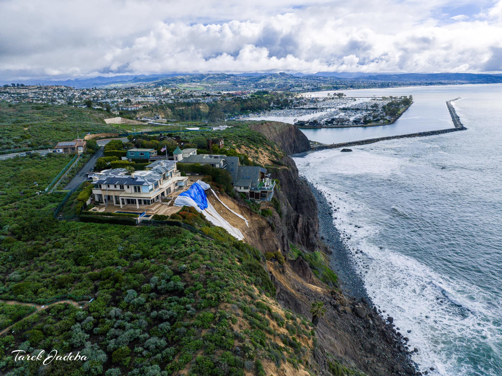 Cliffside home stabilized with tarps after coastal landslide near oceanfront.