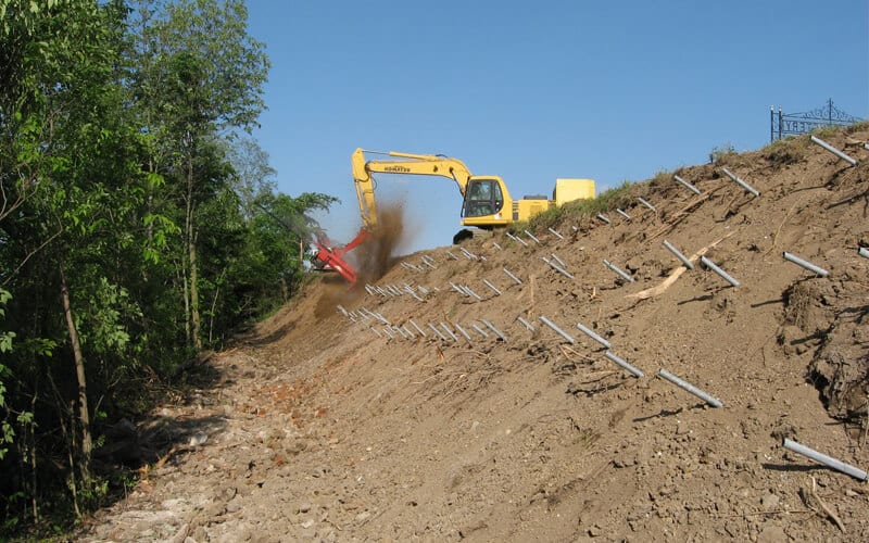 Excavator working on a slope with soil nails installed in a grid pattern.