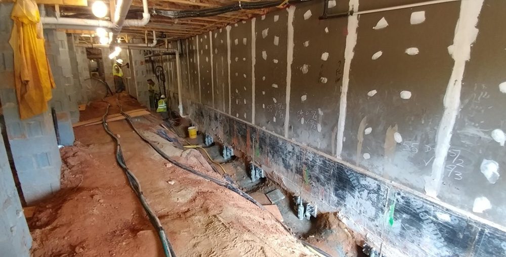 Sinkhole repair showing exposed soil and support piers along a wall.