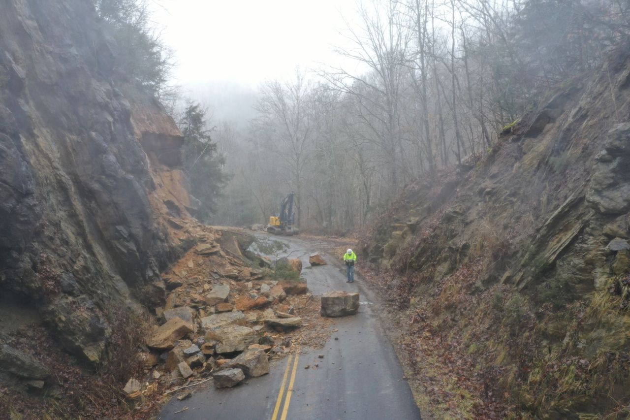 Rockfall debris blocking a road with workers and equipment beginning cleanup and mitigation efforts.
