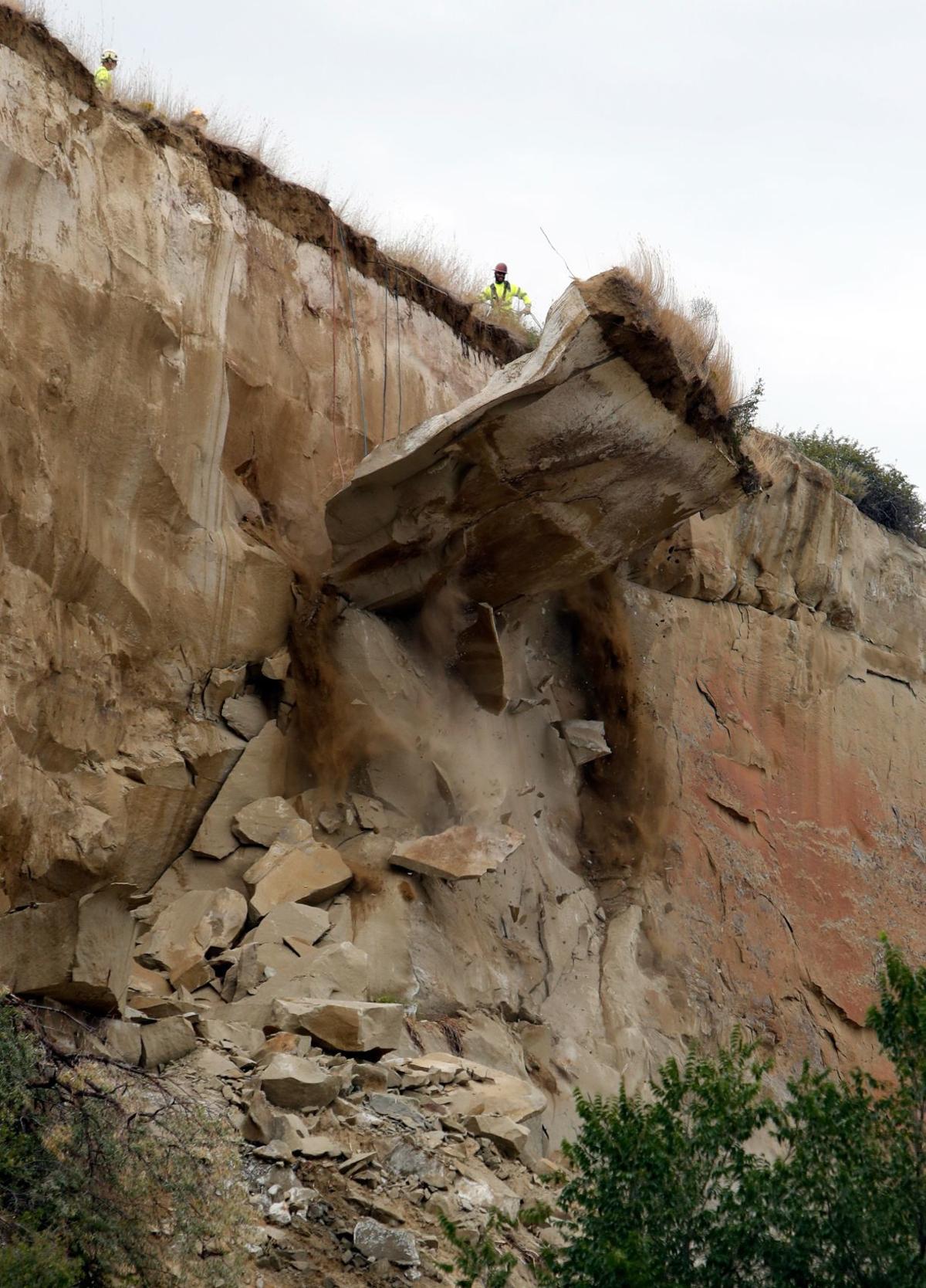 Large rock slab falls from a cliff as a worker observes from above.