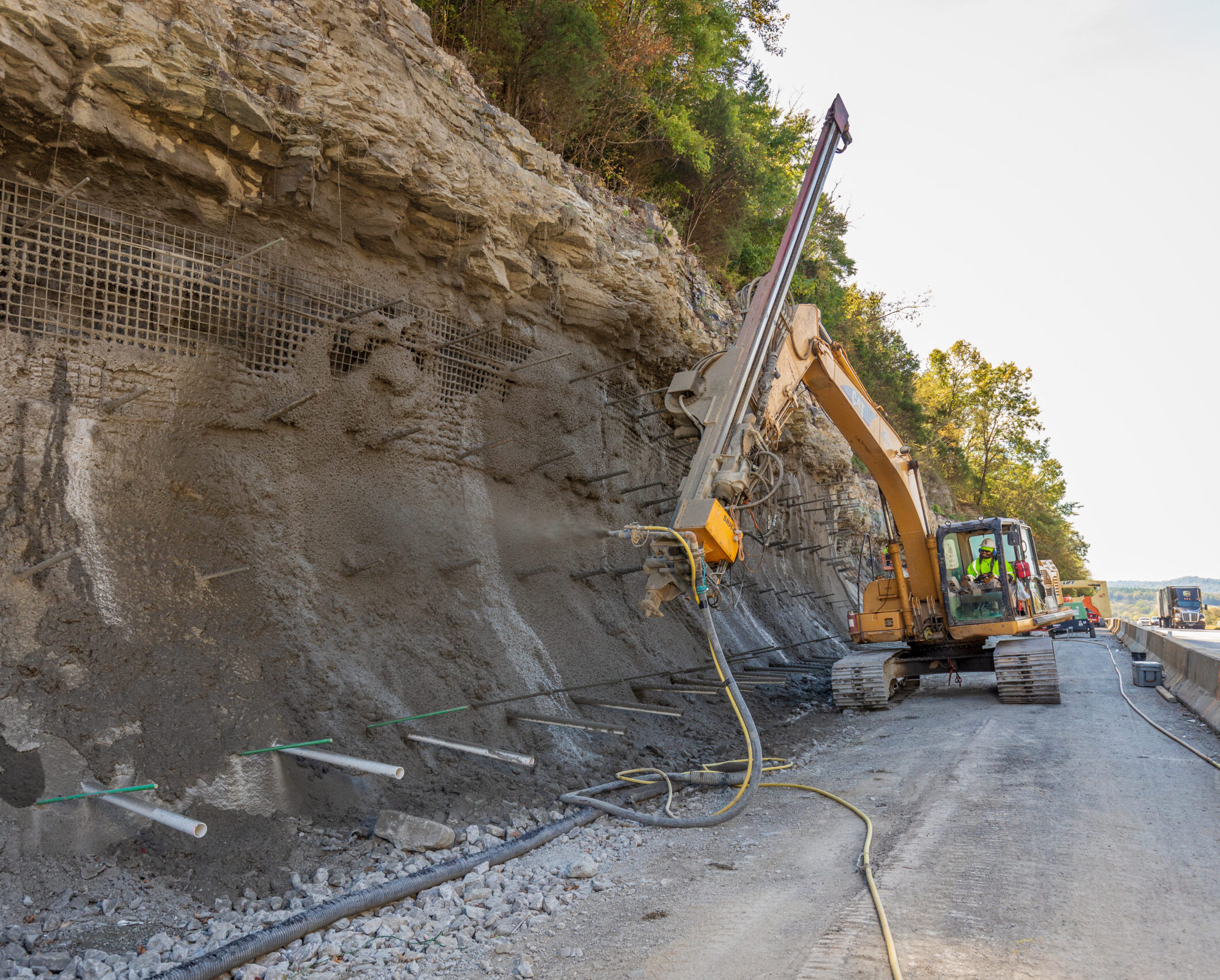 Shotcrete robot applying concrete to a roadside slope.