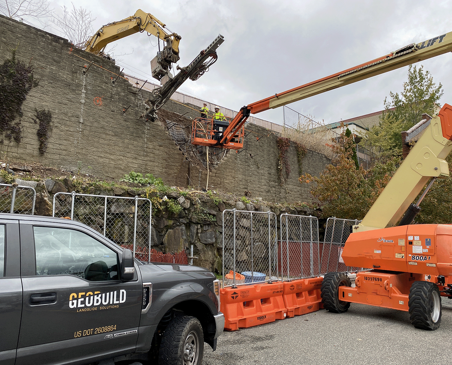 Crew using lifts and a drill attachment to stabilize a tall retaining wall.