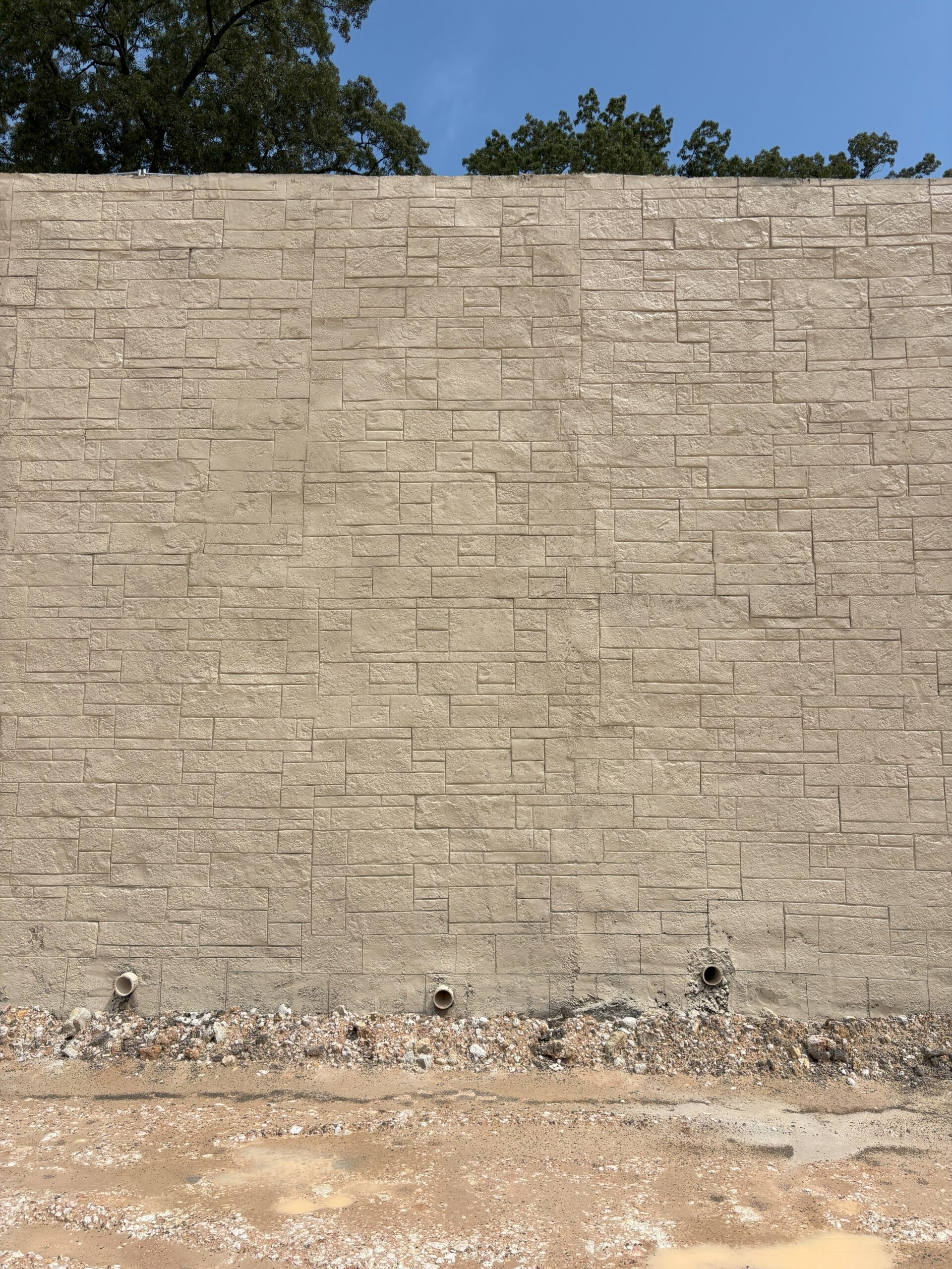 Vertical shotcrete wall featuring a stamped ashlar stone pattern in a light beige finish.
