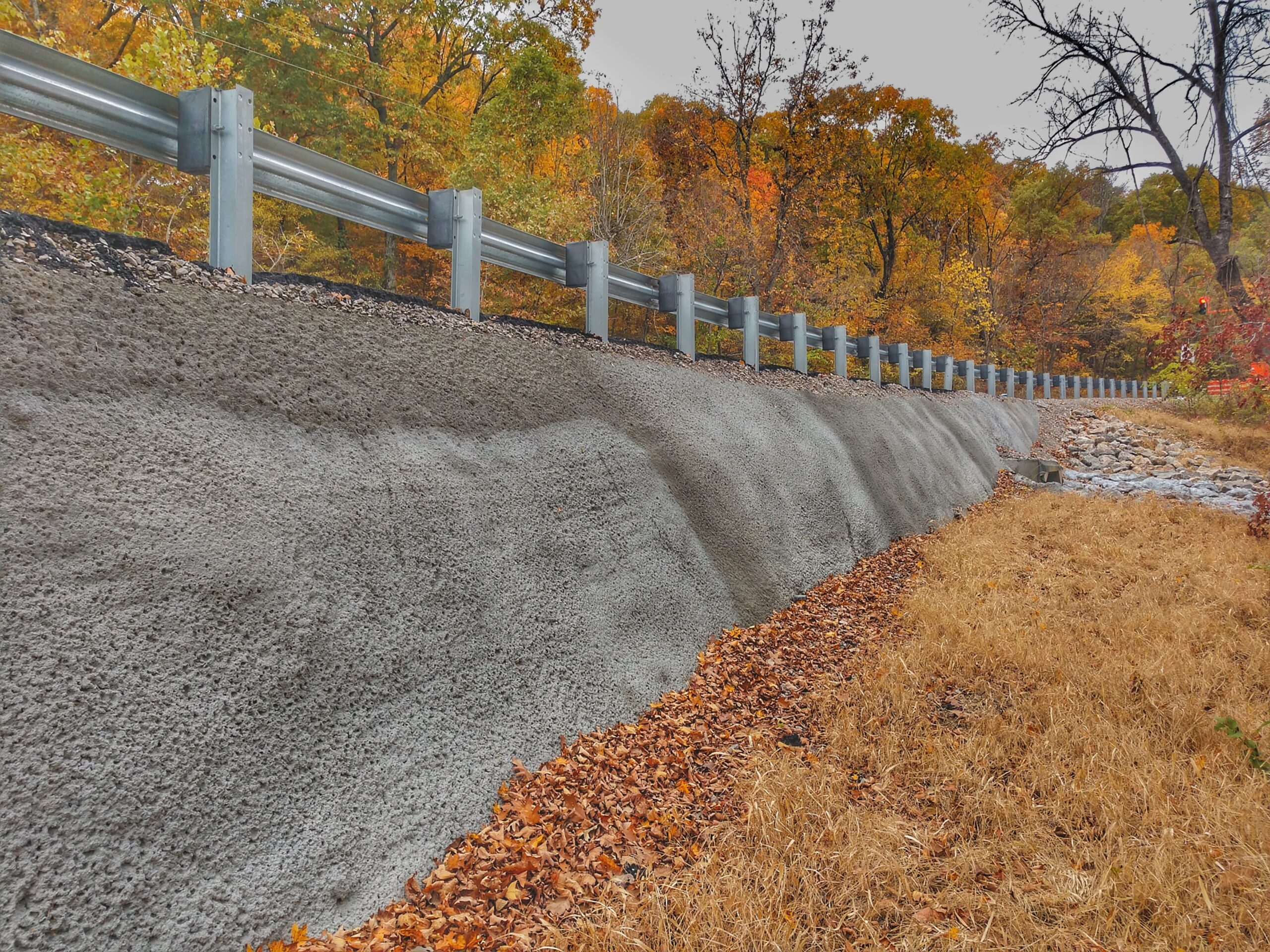 Roadside shotcrete wall with rough-gun finish beneath a guardrail.