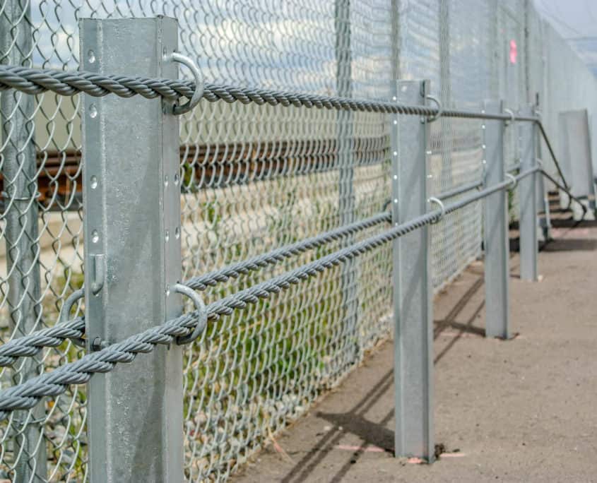 Galvanized cable barrier with chain link fence panel on steel posts along a paved surface
