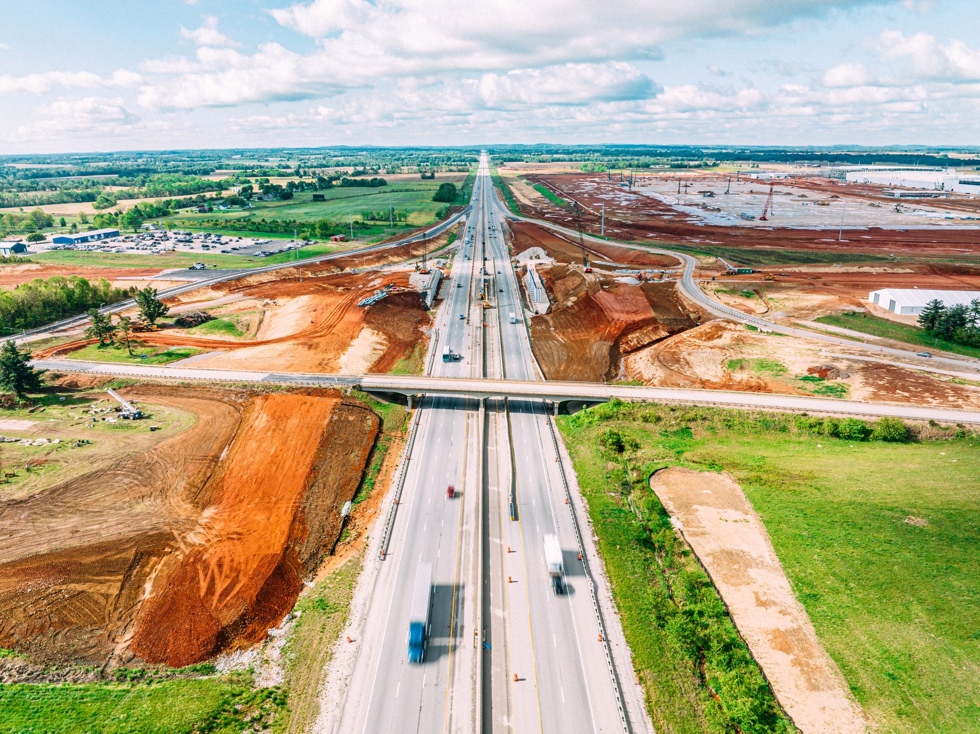 Aerial view of major interstate highway interchange under construction with graded earthwork and overpass bridge