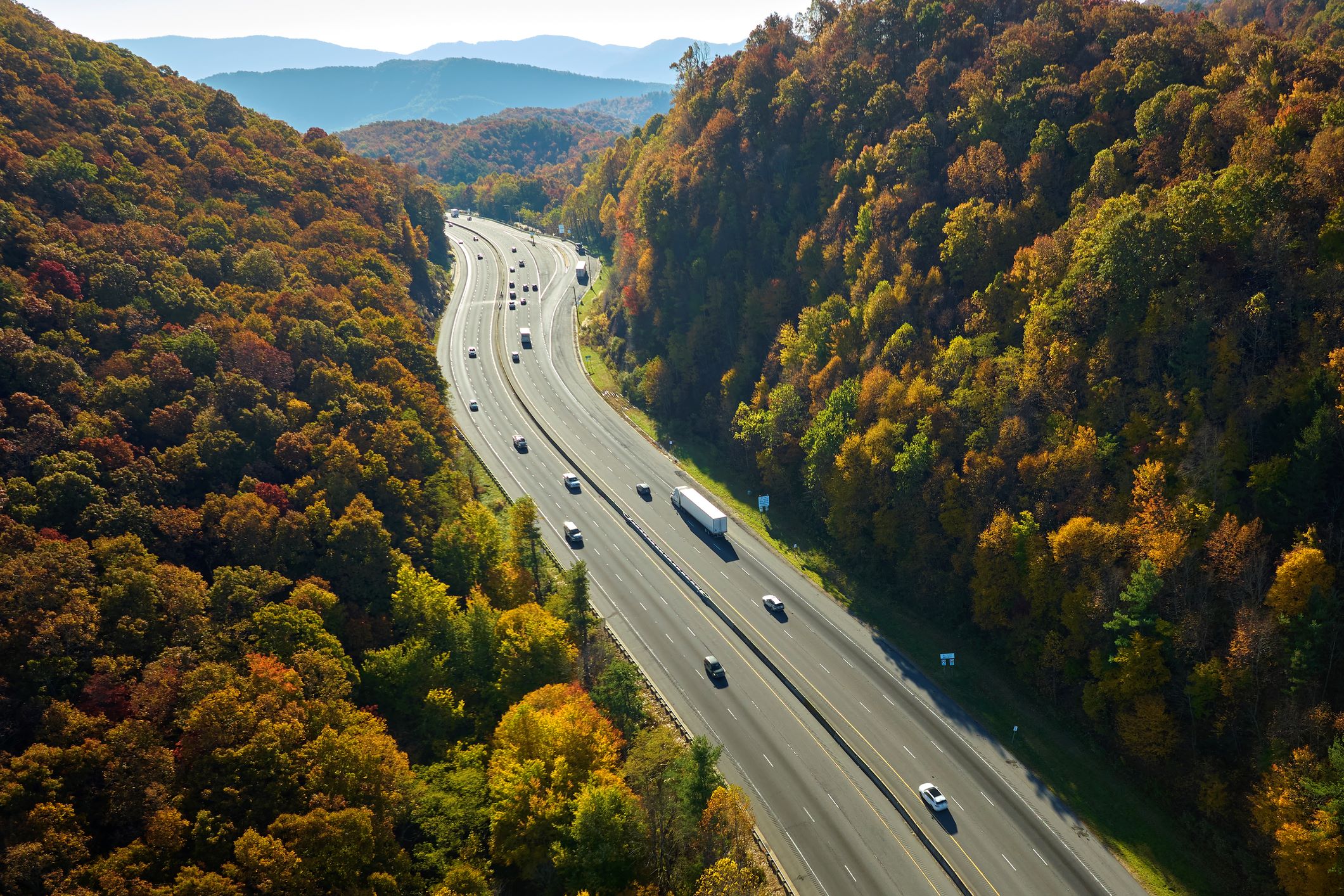 Aerial view of multi-lane interstate highway through autumn mountain forest with cable barrier median