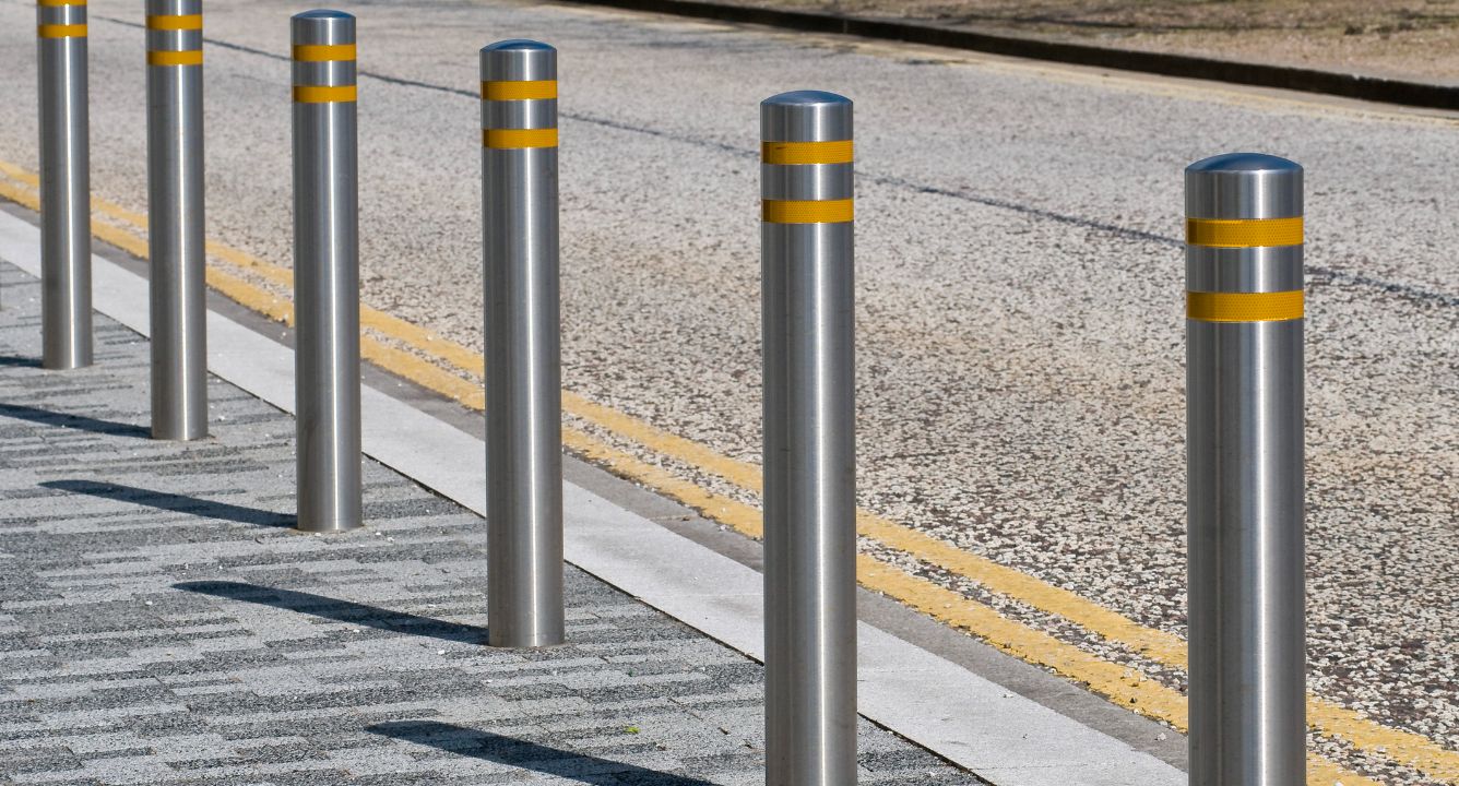 Row of stainless steel bollards with yellow reflective bands lining a pedestrian walkway