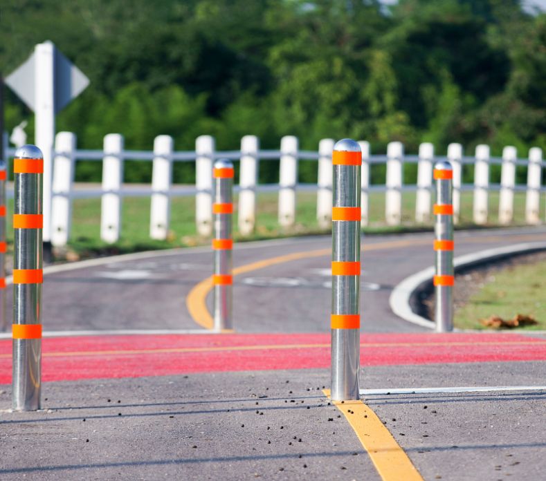 Stainless steel bollards with orange reflective bands separating a bike lane from a road