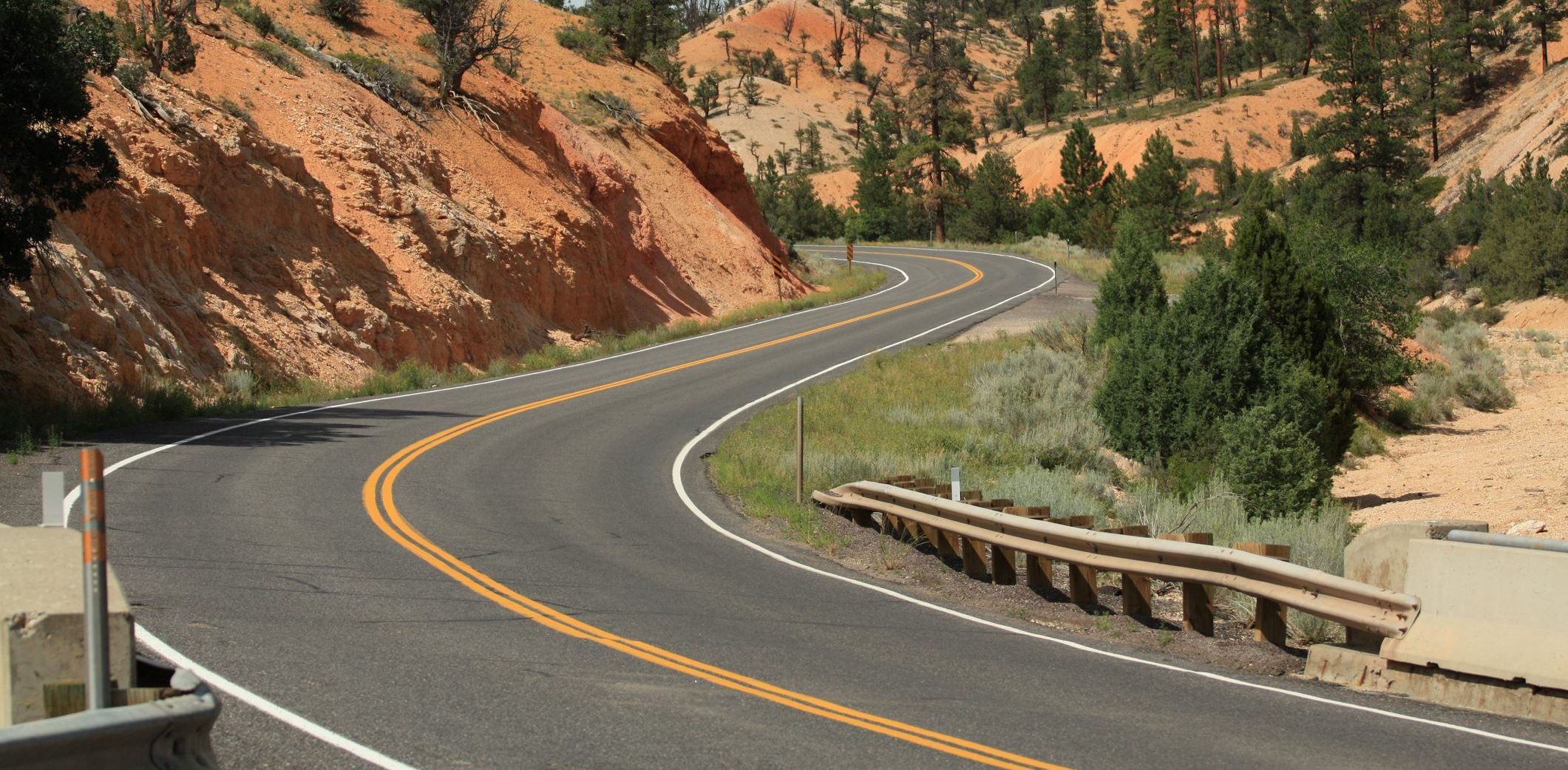 W-beam guardrail on a winding two-lane highway through red rock desert canyon terrain