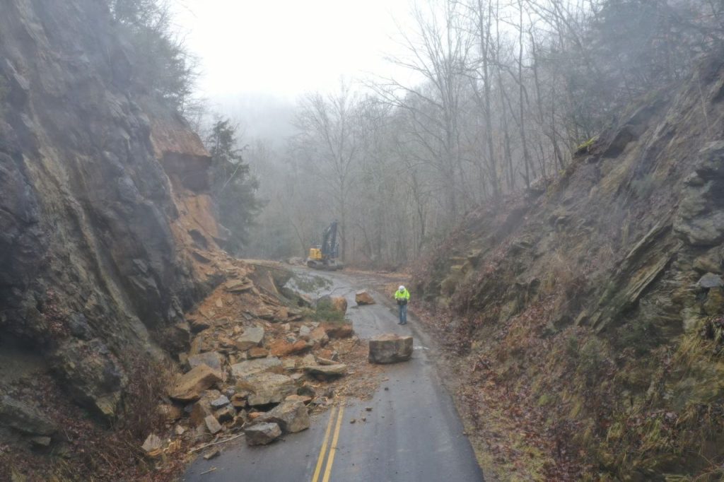 Rockfall debris blocking a road with workers and equipment beginning cleanup and mitigation efforts.