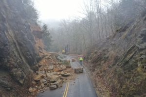 Rockfall debris blocking a road with workers and equipment beginning cleanup and mitigation efforts.