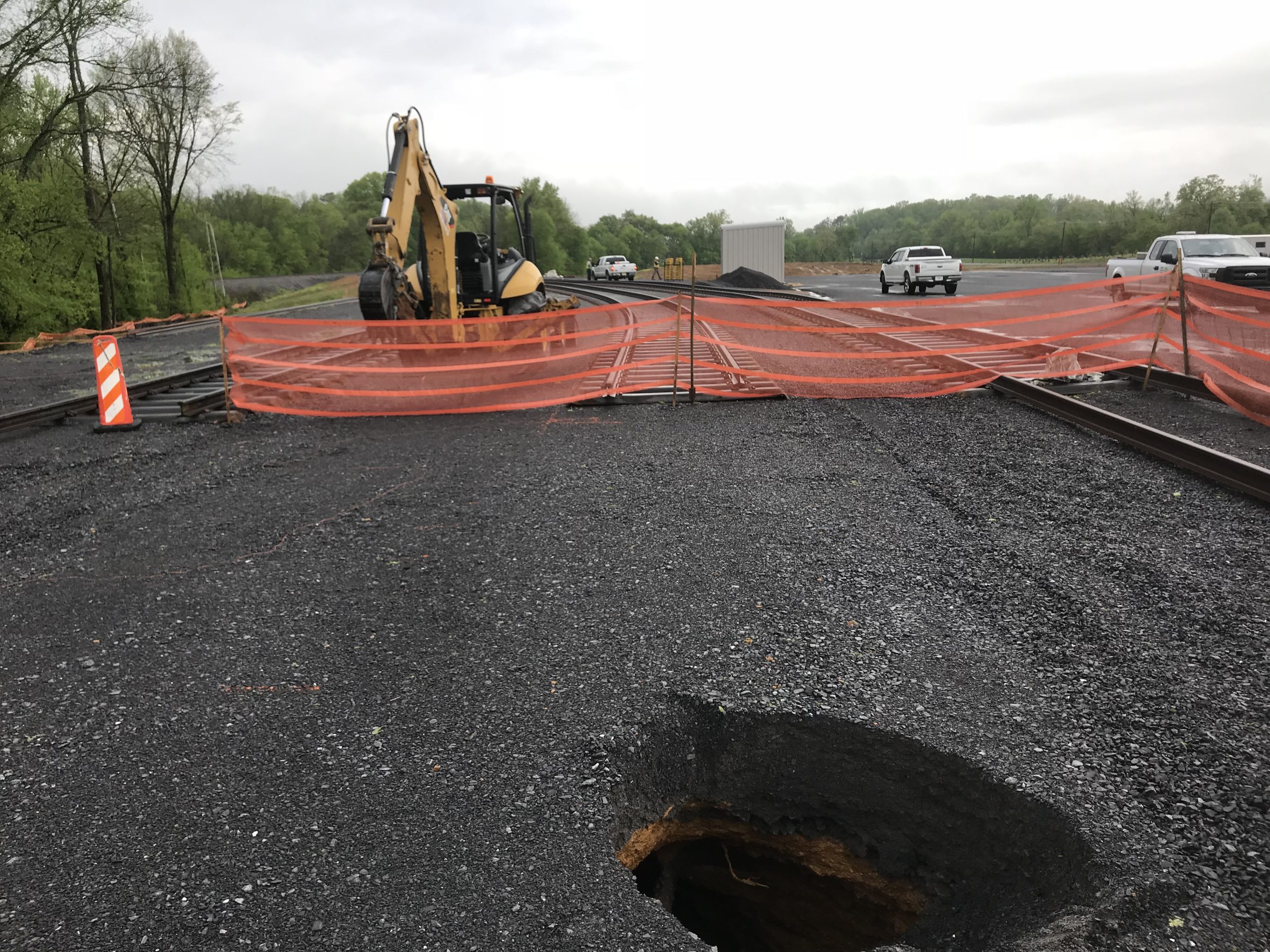 Sinkhole near a construction zone with an excavator and orange safety fencing.