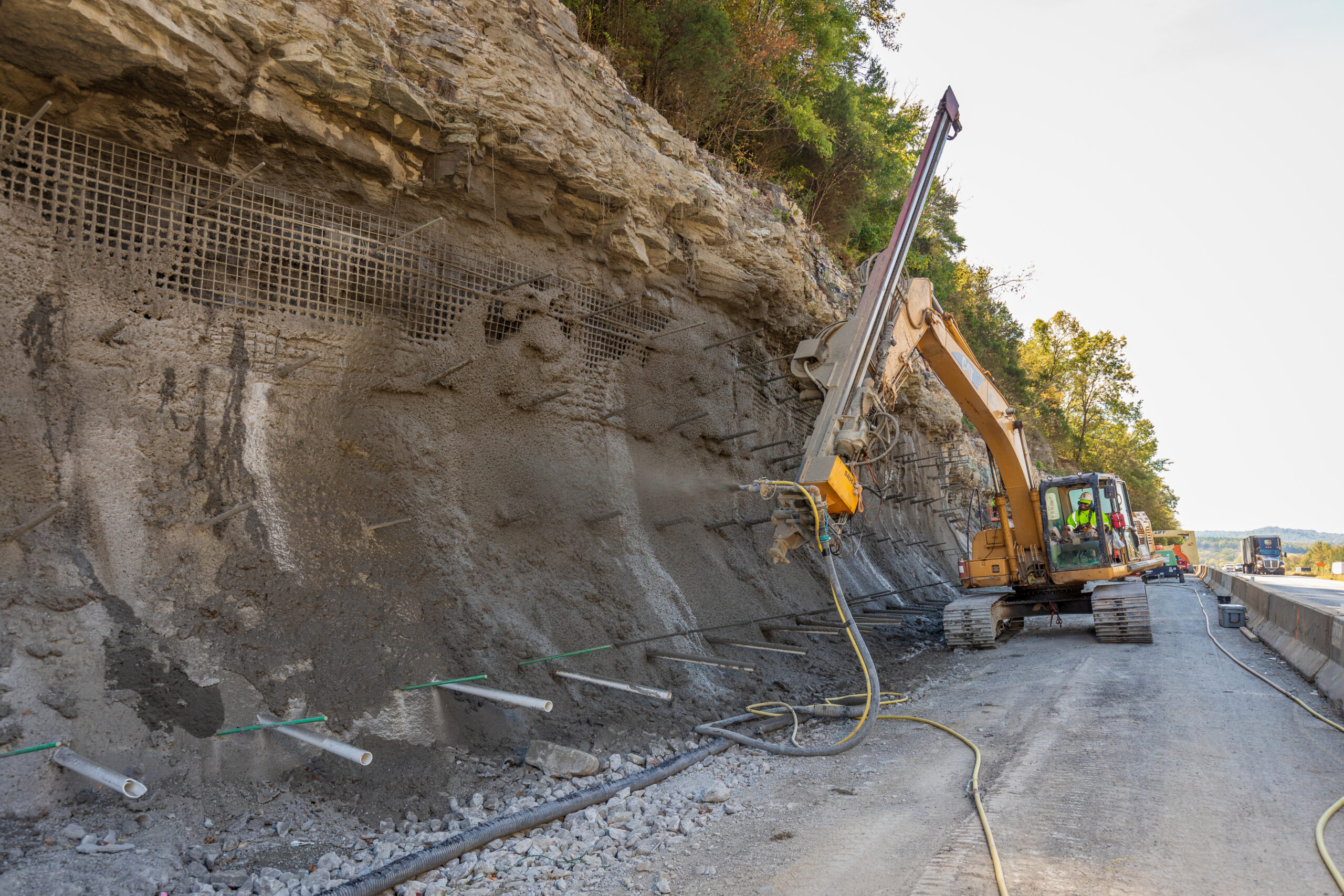 Shotcrete robot applying concrete to a roadside slope.