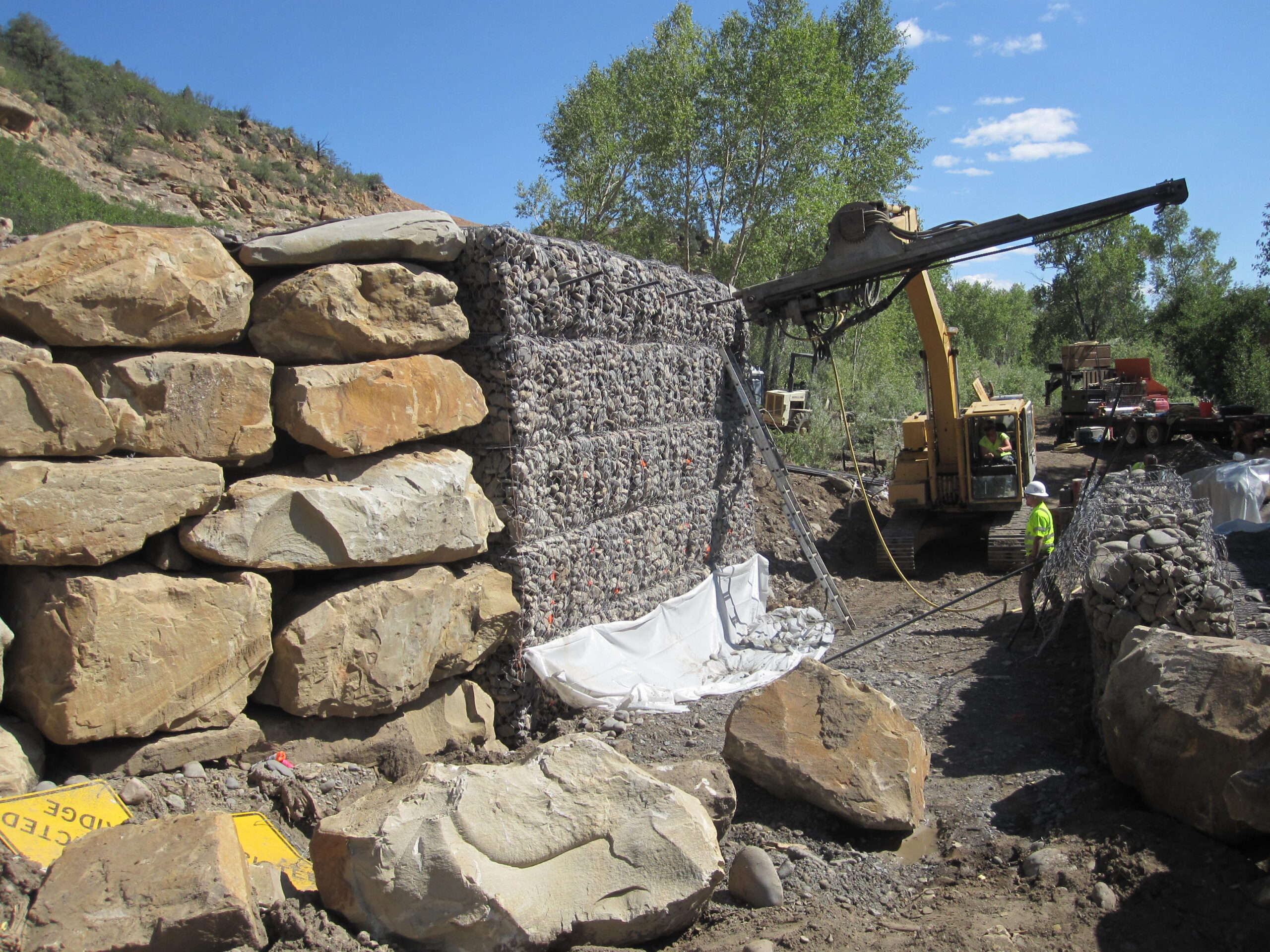 Construction crew using drilling equipment to stabilize a MSE wall.