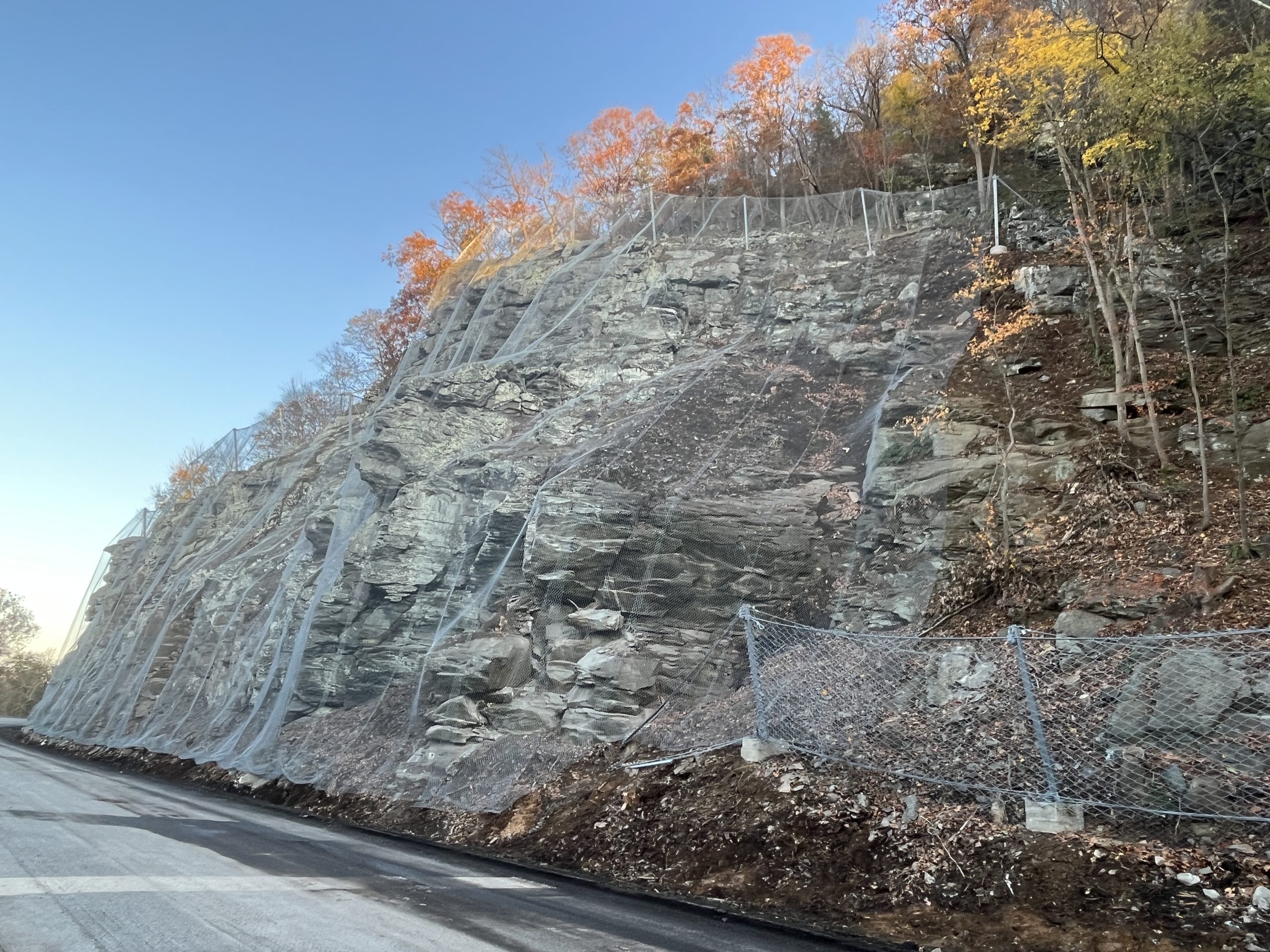 Rock slope alongside roadway secured with rockfall mesh and bolts.