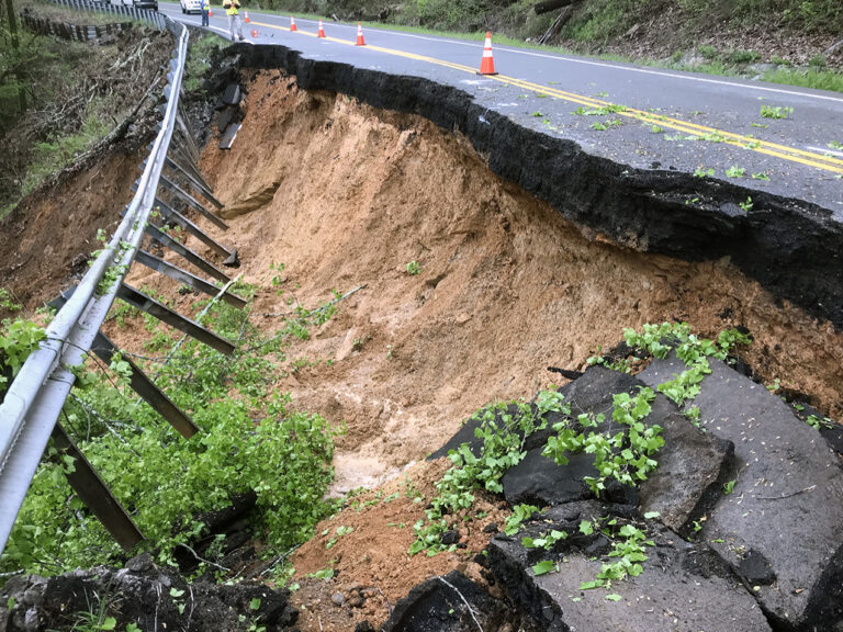 Collapsed roadway with guardrail damaged by a landslide exposing soil beneath.
