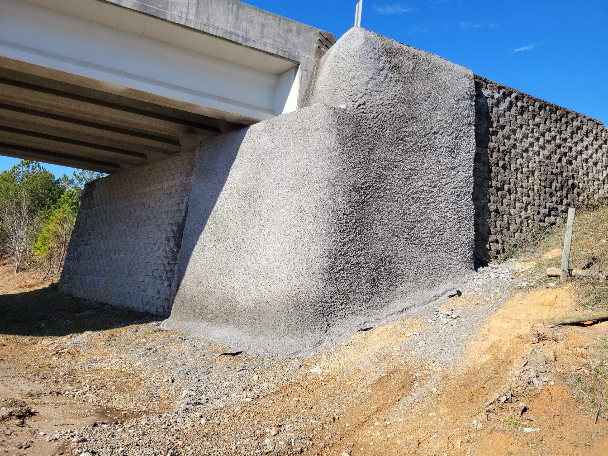 Bridge abutment stabilized with shotcrete and retaining wall beneath roadway.