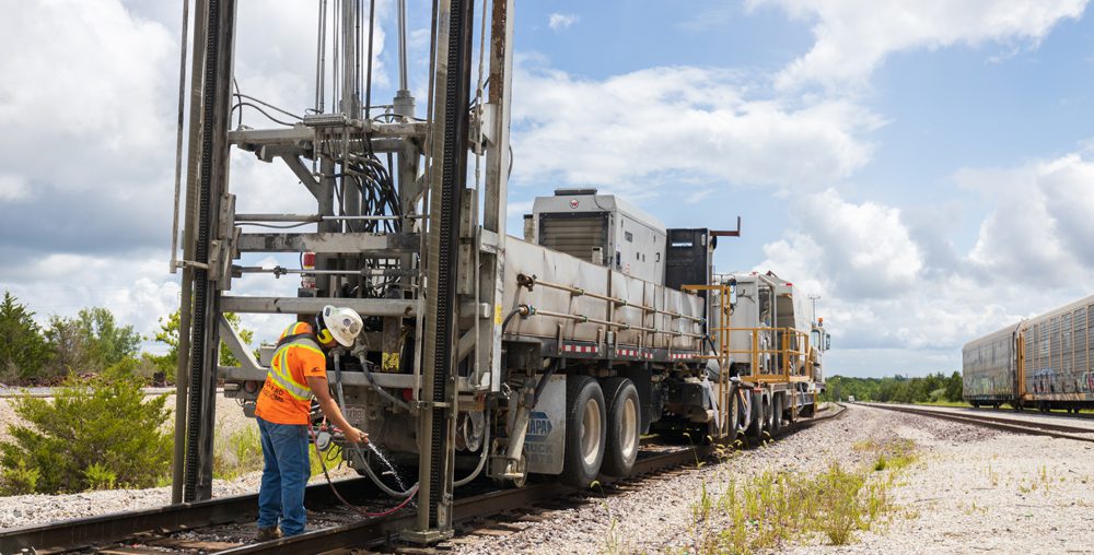 Worker operating RailJET drilling equipment on a railroad track.