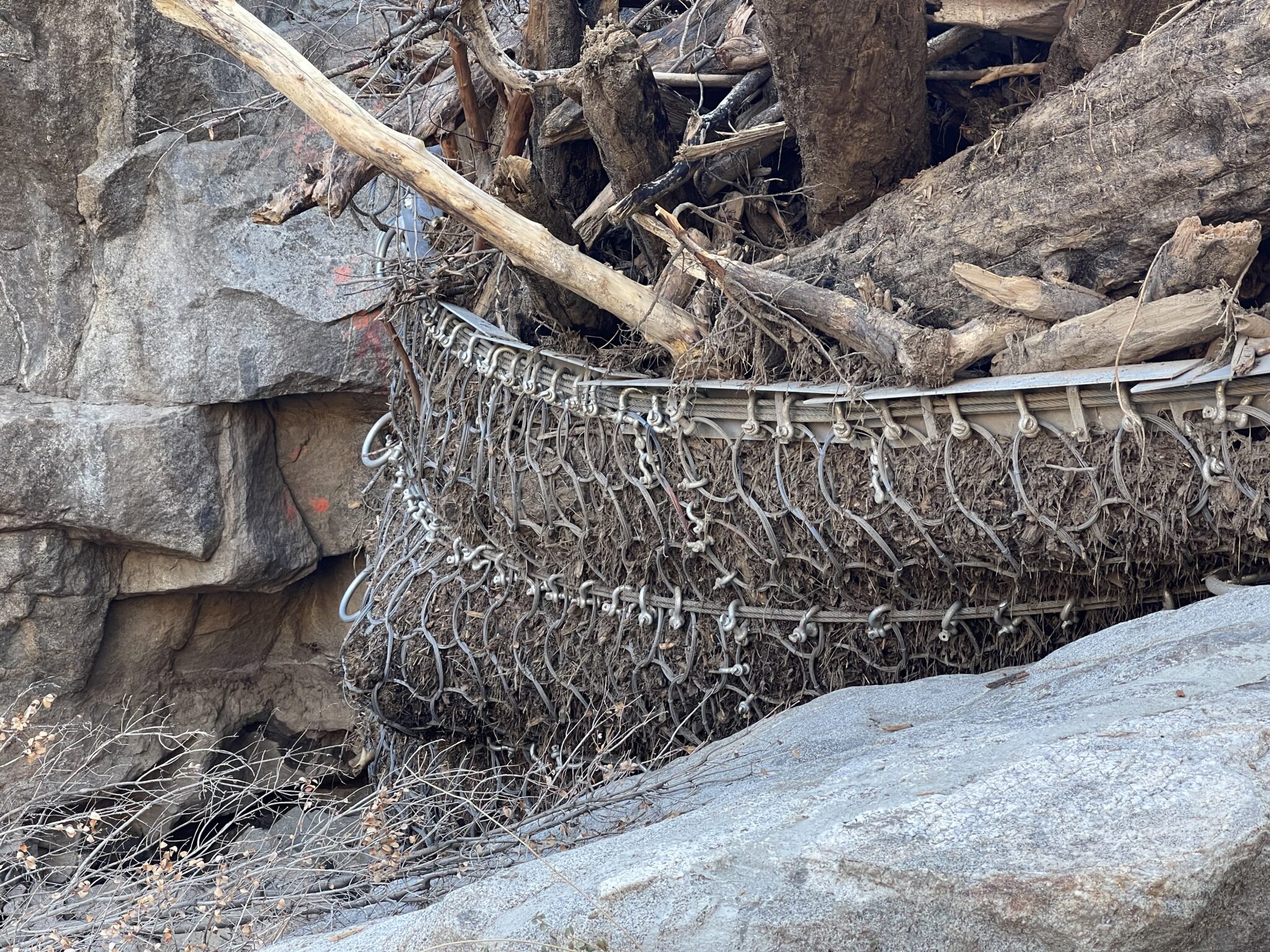 Rockfall barrier catching large debris and tree branches.