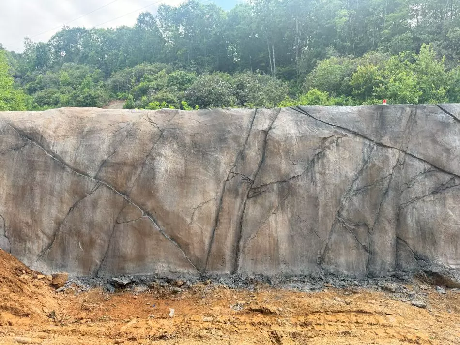 A finished shotcrete retaining wall with a sculpted, textured finish blending into a natural landscape for slope stabilization.